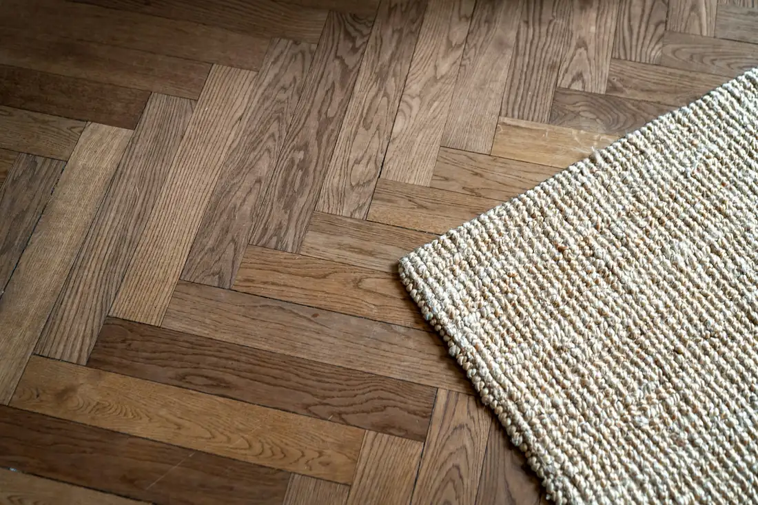 Parquet en bâtons rompus, fil du bois bien visible, coin d’un tapis en jute