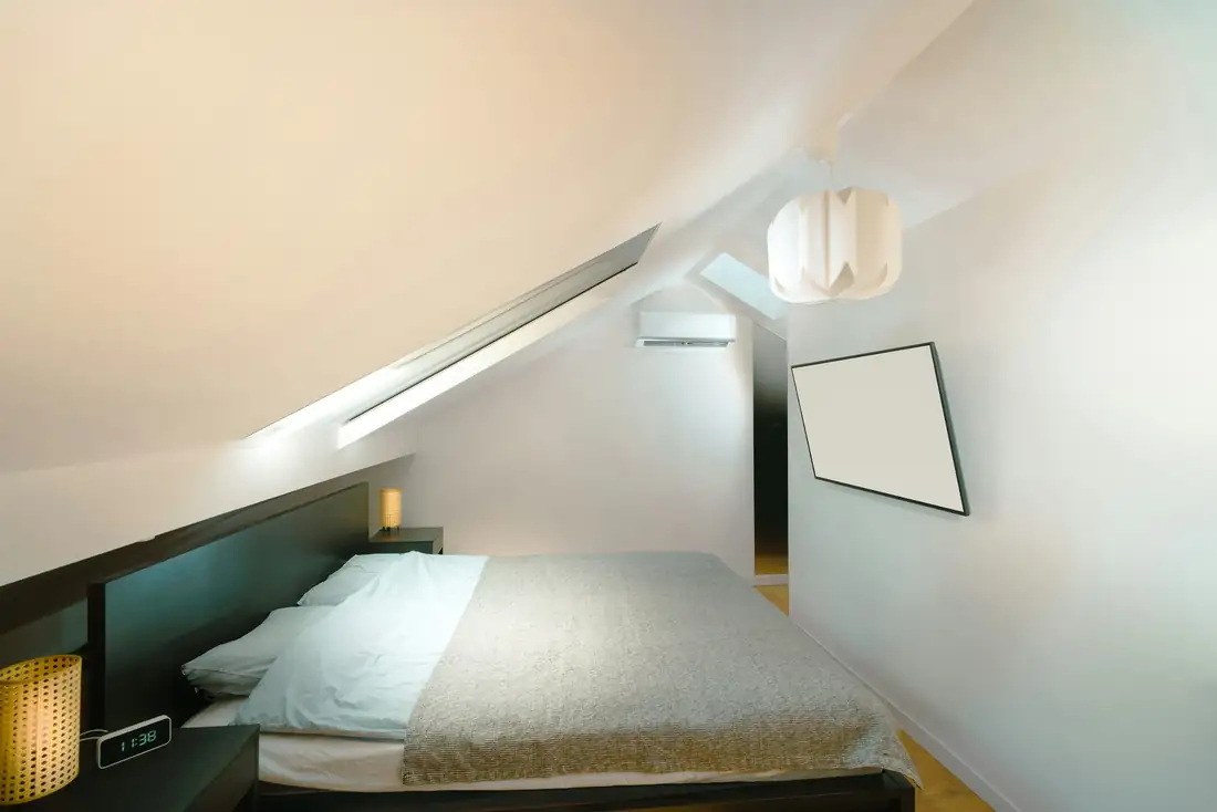 Chambre aménagée sous une pente de toit, murs blancs et lit bas