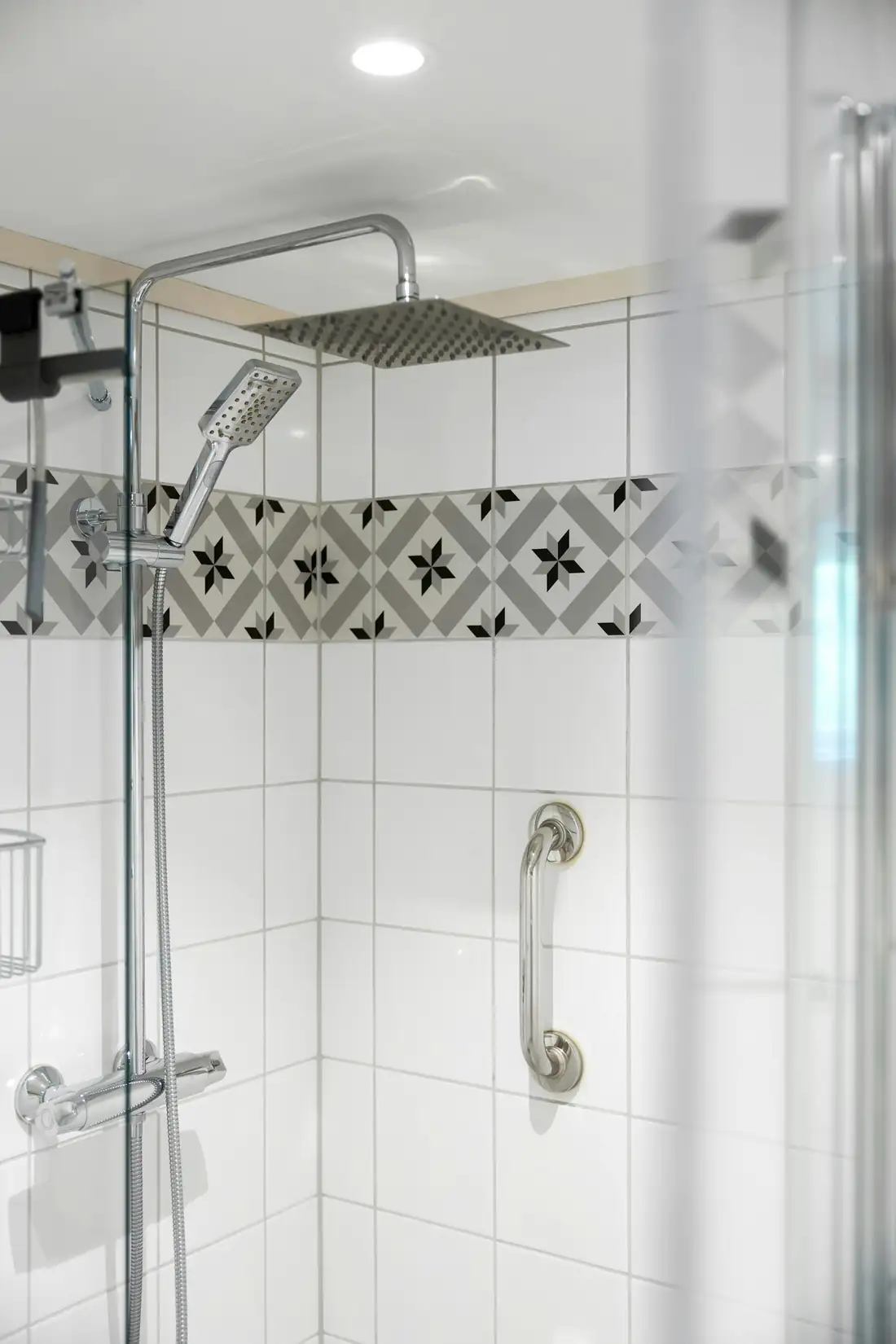 Douche carrelée de blanc avec pomme de tête, mitigeur et barre d’appui