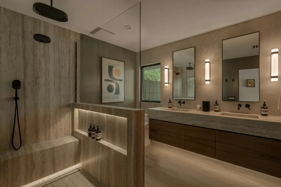 Salle de bain en pierre beige : douche ouverte à gauche, double vasque et meuble en bois à droite