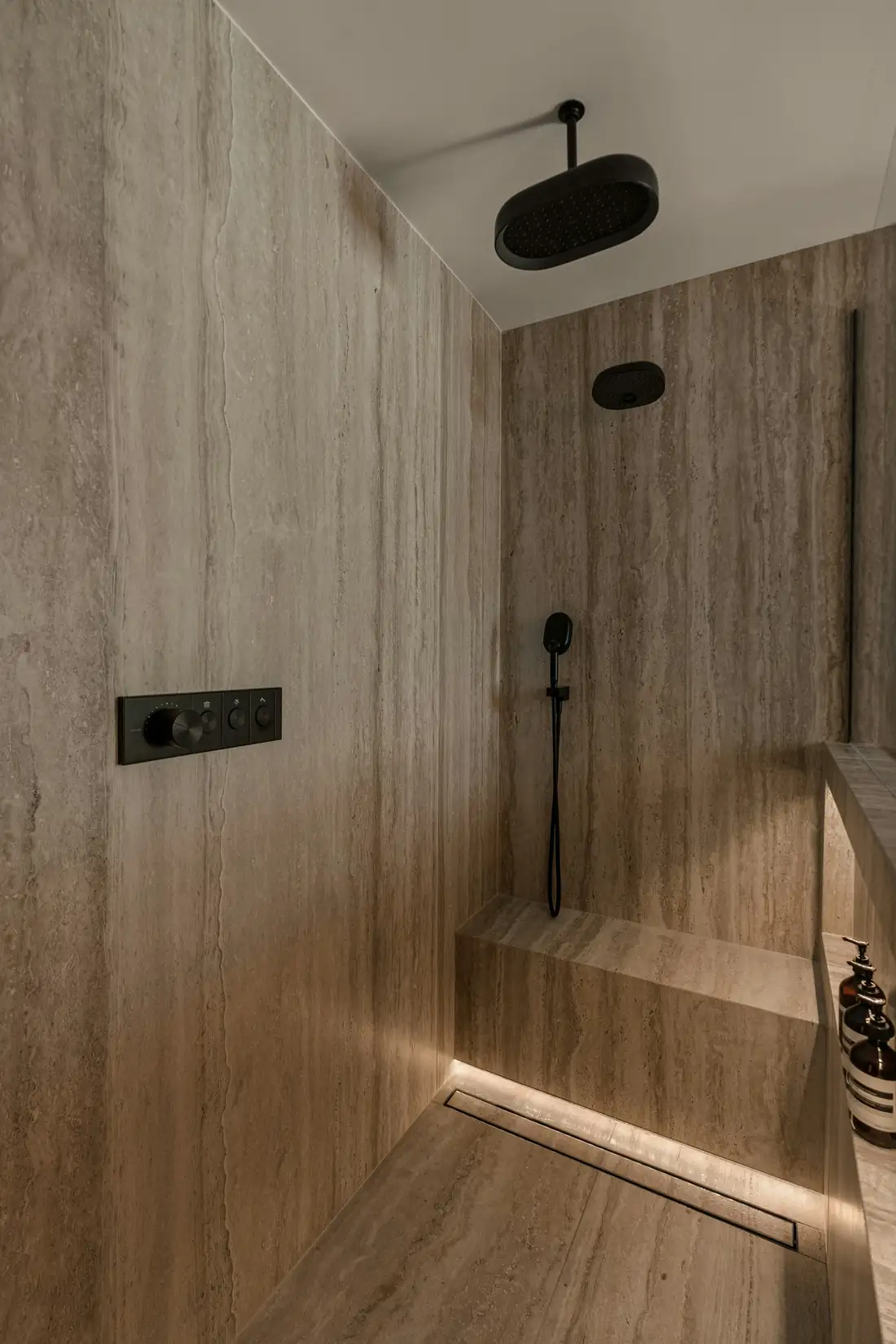 Douche de plain-pied habillée de pierre claire, banc maçonné et pomme de douche au plafond