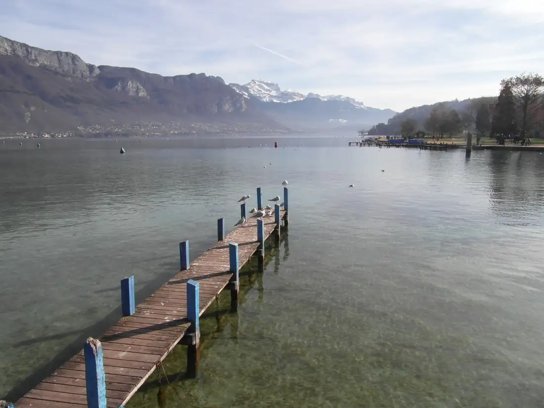 Le lac d’Annecy vu du Pâquier : un ponton de bois s’avance dans l’eau calme, montagnes au fond