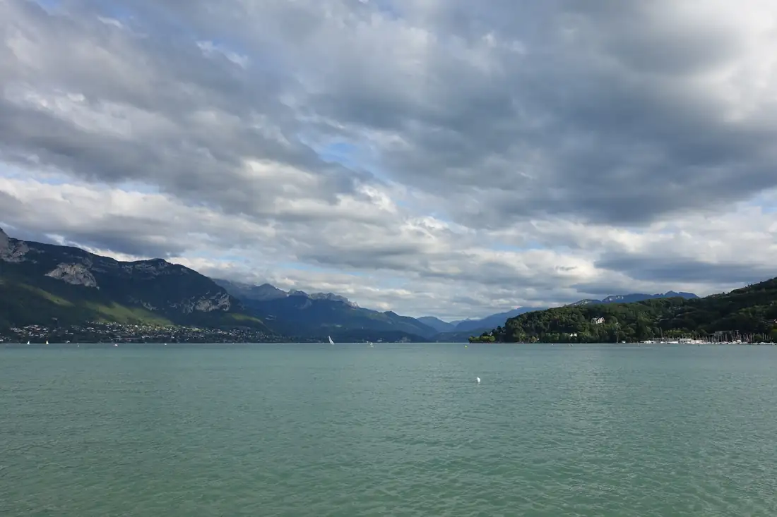 Vue large du lac d’Annecy sous un ciel chargé, rives boisées et montagnes