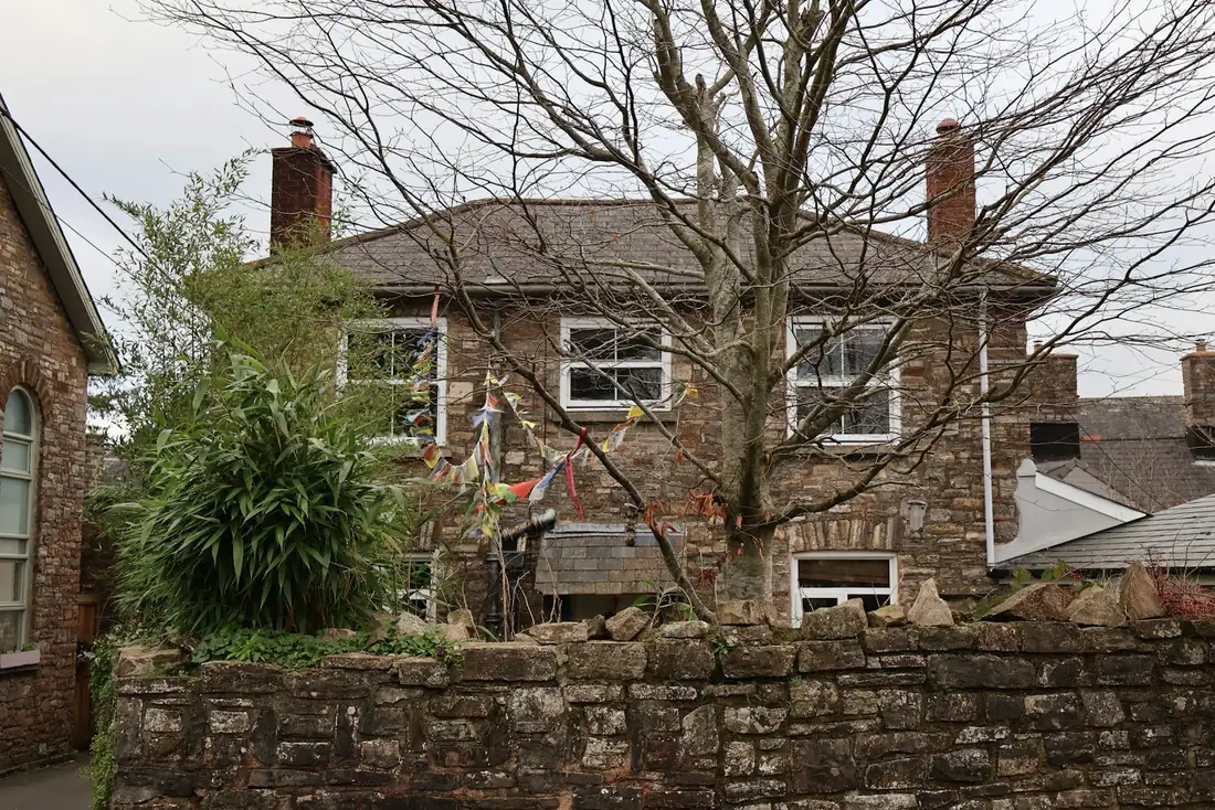 Maison ancienne aux fenêtres blanches, muret de pierre au premier plan