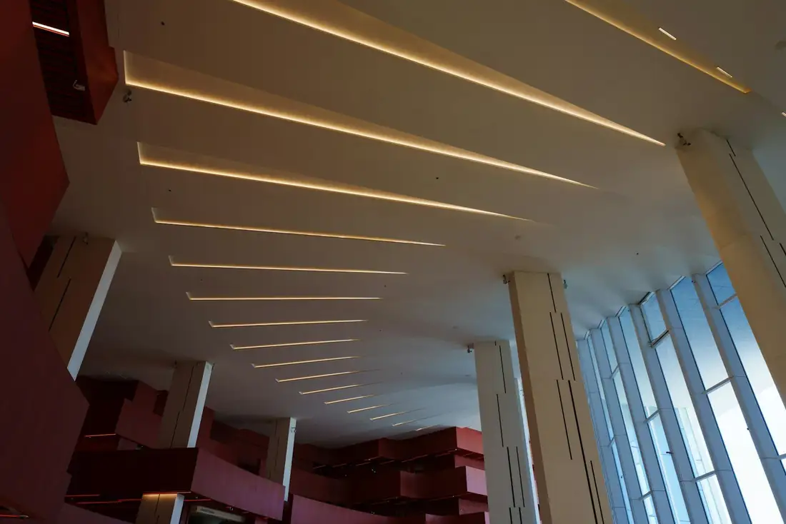 Plafond blanc traversé de lignes lumineuses encastrées, grande baie sur le côté