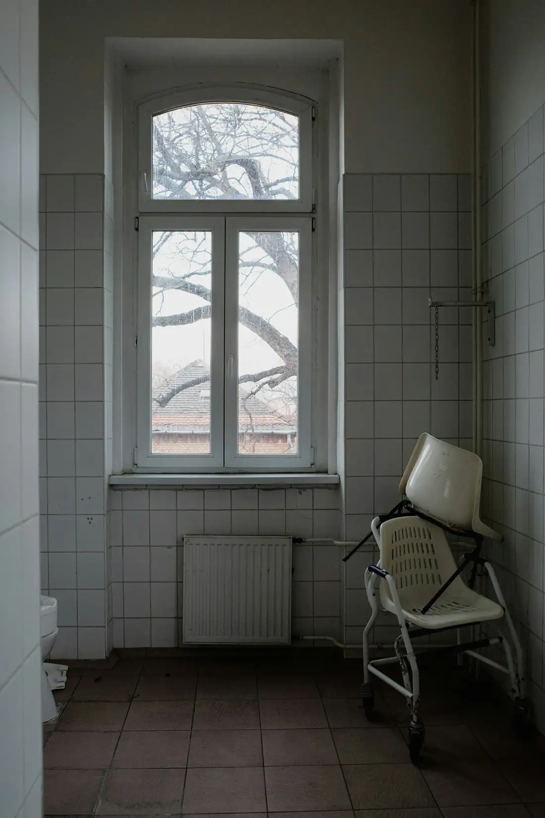 Siège de douche posé sous une fenêtre cintrée dans une salle d’eau carrelée