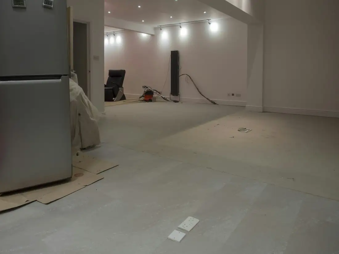 Pièce vide en travaux, sol gris préparé et spots allumés au plafond