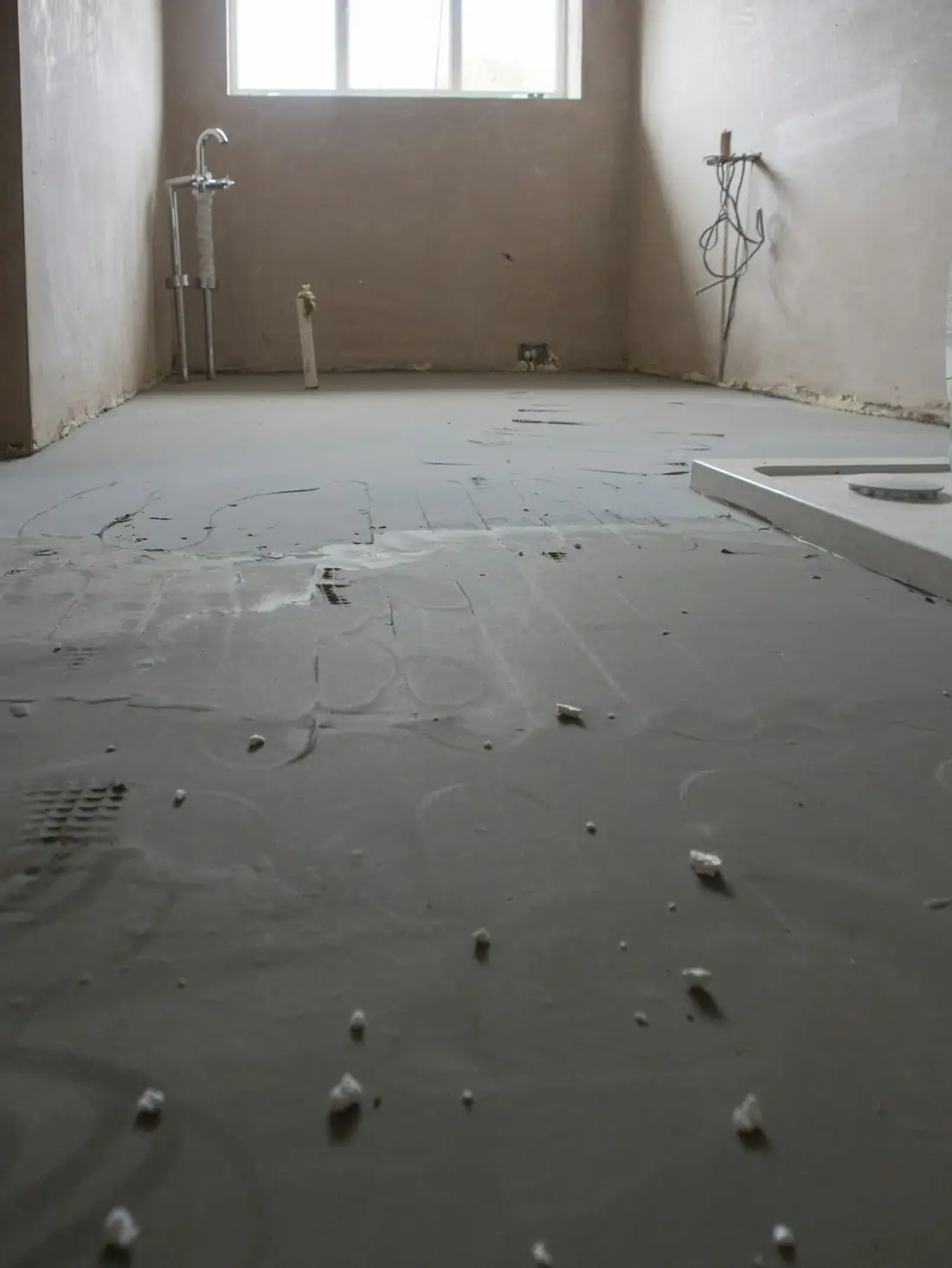 Sol de salle d’eau en travaux, enduit de sol gris et attentes de plomberie